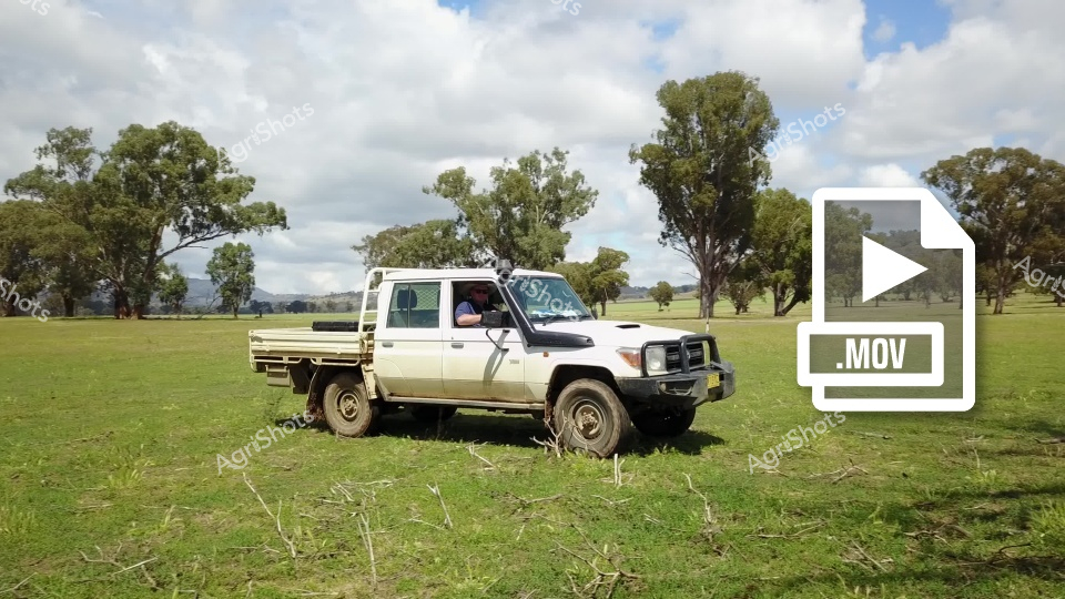 A white Toyota Land Cruiser utility vehicle sits parked on a grassy field with scattered eucalyptus trees in the background. The rugged four-wheel drive truck, typical of Australian rural and agricultural settings, appears well-maintained and positioned in an open pastoral landscape under a cloudy sky. The scene suggests a working vehicle used for farm or station operations in a typical Australian countryside environment.