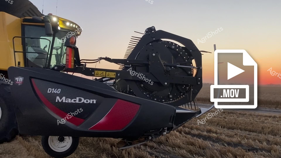 A powerful MacDon D140 harvester works at sunset, capturing the golden light across a wheat field in New South Wales. The advanced agricultural machinery meticulously collects grain with its large header, representing modern farming technology at work during harvest season.