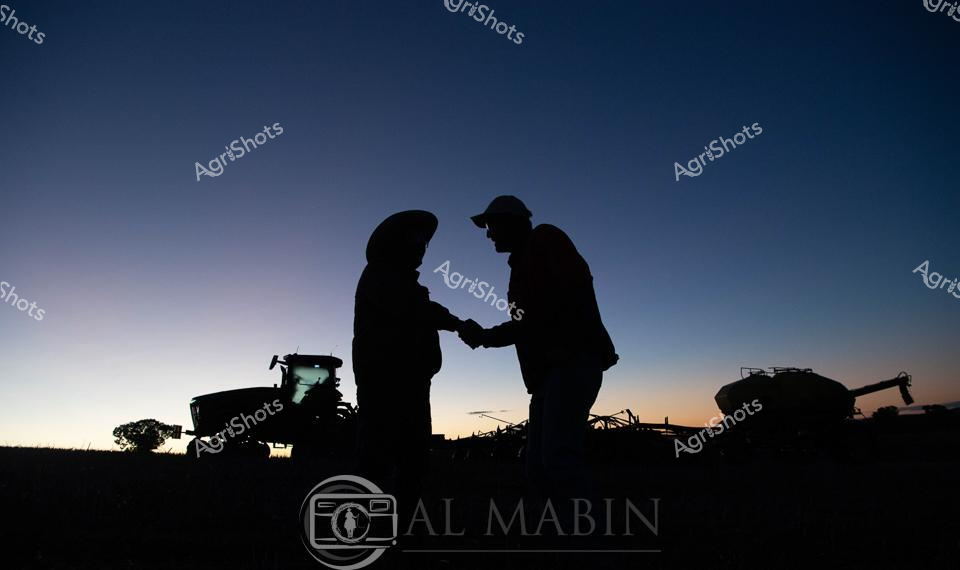 Golden light bleeds across the horizon as two agricultural workers stand in silhouette, sharing a moment of connection amid the rural landscape. A powerful John Deere tractor anchors the scene, its massive form a testament to modern agricultural technology, while an air seeder waits nearby - signaling the critical planting season. The workers' body language suggests a collaborative discussion, perhaps strategizing the day's agricultural tasks or reflecting on the crop's potential. Soft gradients of deep blue and pale amber paint the sky, capturing the tranquil dawn moments before full sunrise - a quintessential Australian agricultural morning that speaks to the rhythm of farming life. Agricultural machinery and human interaction merge in this compelling scene, symbolizing the partnership between human skill and technological innovation that drives rural productivity. The carefully composed silhouettes create a powerful visual narrative of teamwork, preparation, and the quiet determination that defines agricultural work.