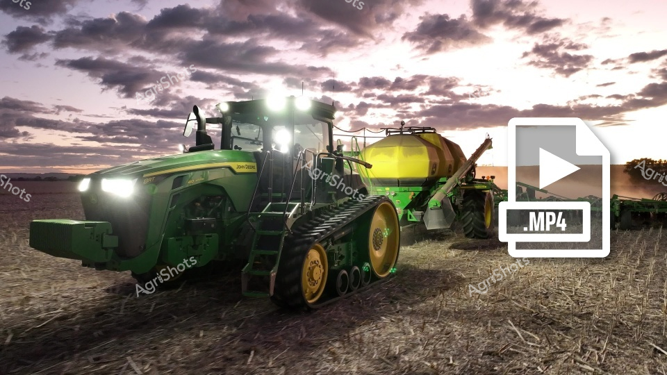 A powerful John Deere tractor with tracked wheels stands ready for seeding operations at sunrise in Western Australia. The agricultural machinery, equipped with an air cart, sits poised in a harvested field under a dramatic cloudy sky, capturing the essence of modern crop production.