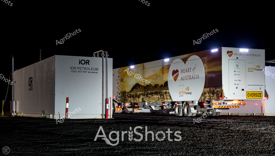 Night falls on a remote industrial transport yard, illuminated by stark overhead lighting that casts dramatic shadows across large transport vehicles. Two massive trailers stand side-by-side - one branded with "IOR Petroleum" in crisp white lettering, and the other adorned with the vibrant "Heart of Australia" mobile healthcare initiative graphics. The "Heart of Australia" trailer, part of an innovative rural healthcare program, features a striking graphic of a landscape silhouette and the organization's heart-shaped logo, signaling its mission to deliver specialized medical services to remote communities.

The oversized trailers represent critical infrastructure for regional Queensland, highlighting the interconnected nature of resource industries and community services. The "OVERSIZE" warning on the trailer underscores the specialized nature of these mobile units, designed to traverse challenging outback terrain. Gravel and industrial infrastructure frame the scene, suggesting a rugged operational environment where logistics and healthcare converge.

The nighttime setting creates a sense of constant movement and purpose, with the illuminated vehicles appearing ready to dispatch essential petroleum resources or medical services across the expansive Australian landscape. This image captures the resilience and innovation required to support remote communities, where distance and isolation demand creative solutions.