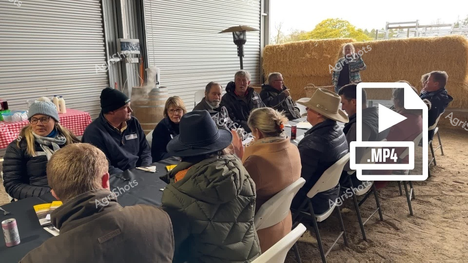 A group of agricultural professionals gather for a safety seminar in a farm setting, with participants seated around tables in a barn-like environment. The attendees, dressed in warm winter clothing, appear engaged in discussion, representing a diverse mix of men and women from the agricultural community in New South Wales or New England region. The meeting seems focused on collaborative learning and safety practices in farming.