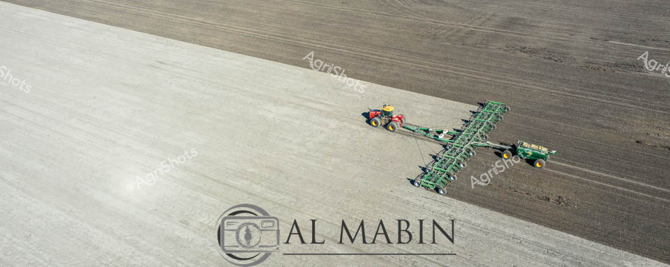 Sweeping across the expansive agricultural landscape, a vibrant yellow and blue tractor pulls an extensive green air seeder, choreographing precision agriculture against a canvas of textured earth. The aerial perspective reveals the immense scale of modern farming, where advanced machinery transforms raw paddocks into potential wheat fields with calculated, GPS-guided movements. Shades of light and dark earth create a stark geometric contrast, highlighting the methodical path of the agricultural implement as it traverses the undulating terrain. The meticulously designed air seeder, with its complex frame and multiple sections, represents the pinnacle of agricultural engineering - a testament to technological innovation in crop cultivation. The scene embodies a sense of quiet determination, where human ingenuity and mechanical precision work in harmony to prepare the ground for future harvest.