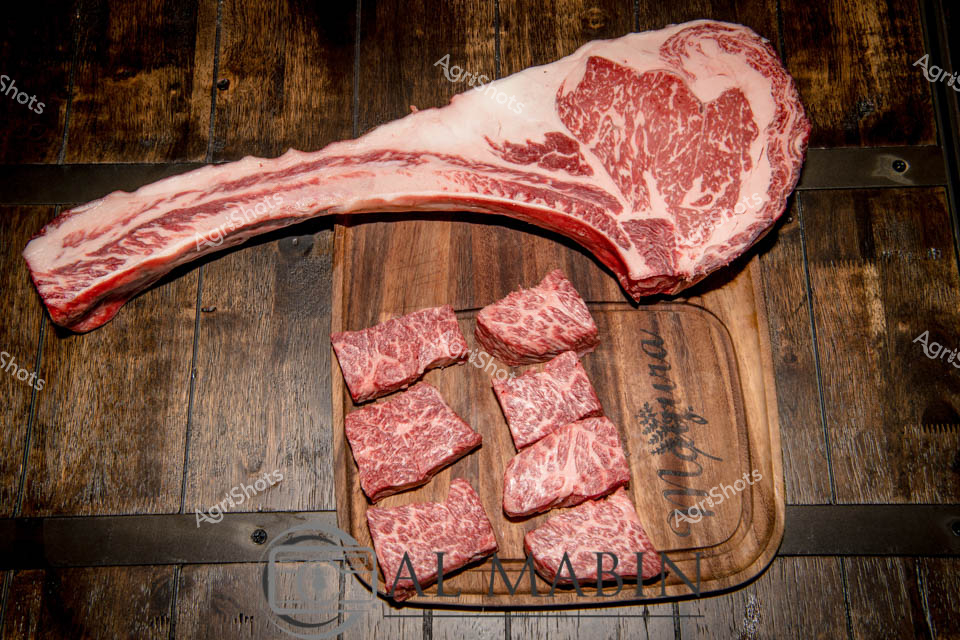 Prime Wagyu beef cuts showcase the exceptional marbling and quality of South Australian livestock production. A massive, curved ribeye steak dominates the wooden cutting board, its intricate white fat veins creating a mesmerizing marble-like pattern against the deep red meat. Surrounding the large cut, several smaller portioned steaks demonstrate the precision and artistry of premium beef preparation. The rich, warm tones of the wooden background and cutting board echo the rustic elegance of high-end culinary presentation, highlighting the premium quality of Mayura Station's Wagyu cattle. Each cut reveals the exceptional intramuscular fat that makes Wagyu beef renowned worldwide, with a delicate, almost painterly distribution of fat that promises exceptional tenderness and flavor. The carefully arranged cuts speak to the meticulous craft of butchery and the pinnacle of Australian agricultural expertise, representing the finest example of beef production from South Australia's premier cattle breeding regions.