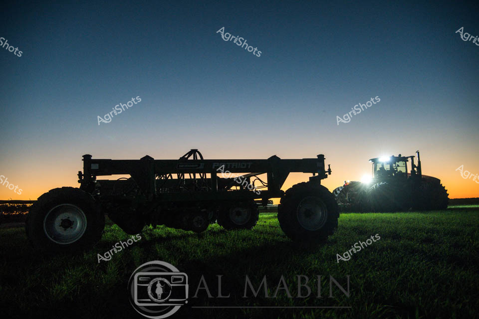 Dusk descends over a pristine Queensland cropping landscape, casting a golden gradient across the horizon as an imposing agricultural air seeder stands silhouetted against the twilight sky. The powerful machine, equipped with expansive tracking wheels and a complex hydraulic boom, represents the pinnacle of modern precision agricultural technology. Illuminated by the tractor's brilliant work lights, the scene captures the quiet moment of agricultural preparation - a testament to the methodical and technologically advanced nature of contemporary farming practices. The rich green grass beneath the machinery provides a vibrant contrast to the deep blue and orange sky, symbolizing the intricate relationship between cutting-edge equipment and the natural environment. This dramatic composition highlights the scale and sophistication of contemporary grain planting operations, where advanced navigation and seeding technologies like Trimble guidance systems enable farmers to work efficiently during the critical twilight hours. The image epitomizes the blend of technological innovation, rural craftsmanship, and the timeless rhythm of agricultural cycles that define Australian farming.
