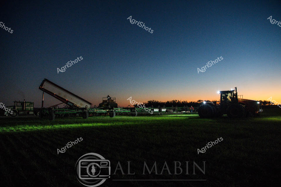 Dawn breaks over a precision agricultural landscape, casting a gradient of deep blues and warm oranges across the horizon. Agricultural machinery stands poised in the early morning light, with a sophisticated air seeder and grain handling equipment positioned strategically across a verdant field. The scene captures the technological sophistication of modern farming, with precision guidance systems and heavy equipment illuminated against the soft glow of sunrise. Large green agricultural vehicles with intricate tracking systems suggest a meticulously planned planting operation, their silhouettes creating a powerful visual narrative of agricultural innovation. The carefully manicured grass beneath the machinery provides a rich, emerald canvas that contrasts beautifully with the deep twilight sky, symbolizing the intersection of natural landscape and advanced farming technology. This image epitomizes the quiet moments of preparation before the day's critical agricultural work begins, representing the cutting-edge agricultural practices of Queensland's farming regions.