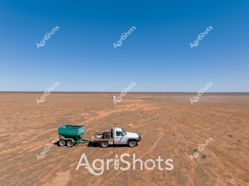 A white utility truck and a green agricultural trailer stand isolated in a vast, arid landscape under a brilliant blue sky. The stark desert environment stretches out to a distant, flat horizon, revealing the challenging terrain of what appears to be an Australian outback region during a severe drought. The reddish-brown earth is parched and cracked, with minimal vegetation, emphasizing the harsh conditions facing rural agricultural operations. The utility vehicle, likely used for farm management or water transportation, sits purposefully on the dry ground, suggesting resilience and adaptation in an unforgiving environment. The green trailer provides a stark contrast to the monochromatic landscape, hinting at the essential mobile infrastructure required to survive in such extreme conditions.

The scene captures the essence of Australian agricultural challenge - survival and persistence in a landscape defined by extreme weather and vast, unforgiving spaces. The solitary vehicle becomes a symbol of human determination against the backdrop of an expansive, uncompromising natural environment.