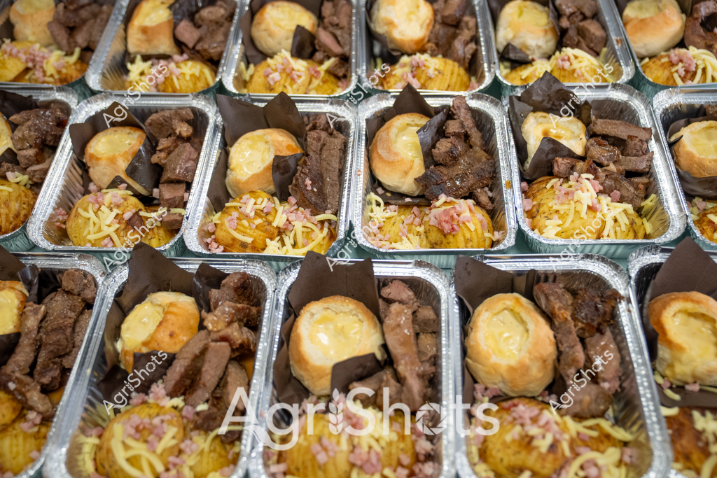 Based on the image and agricultural stock photography guidelines, here's a description:

Precision-prepared meal trays showcase a professional catering setup featuring tender beef portions, golden-brown rolls, and cheese-topped side dishes. Each aluminum container is meticulously arranged with uniformly cut meat pieces, presenting a systematic approach to portion control and food service. The rich brown meat cuts contrast beautifully with the golden-yellow bread rolls and sprinkled cheese garnish, suggesting a carefully planned commercial food preparation process. Multiple identical trays are lined up in a grid pattern, indicating large-scale catering or meal preparation for an event, workplace, or institutional setting. The consistent portioning and professional packaging demonstrate high-quality food service standards typical of Australian commercial food production.

The description focuses on the visual details, systematic arrangement, and professional food preparation aspects, aligning with agricultural and food service stock photography guidelines.